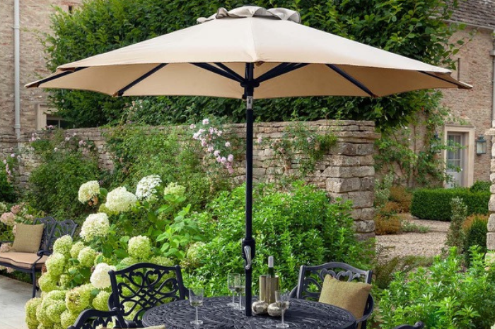 Beige patio umbrella over a table with glasses in a garden setting.