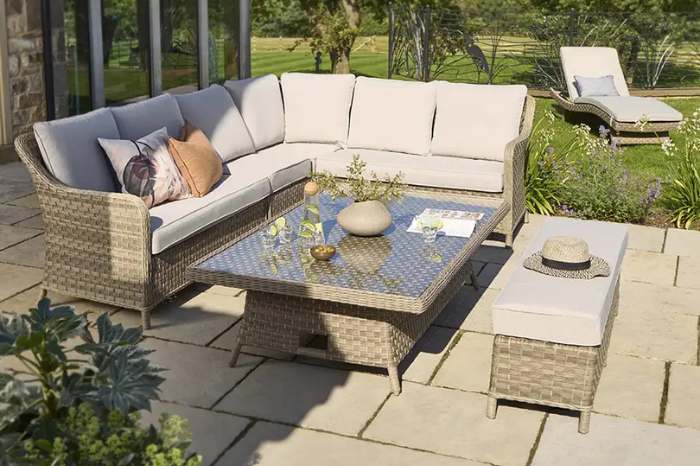 Outdoor rattan corner dining set with cream cushions and adjustable table, styled on a stone terrace.
