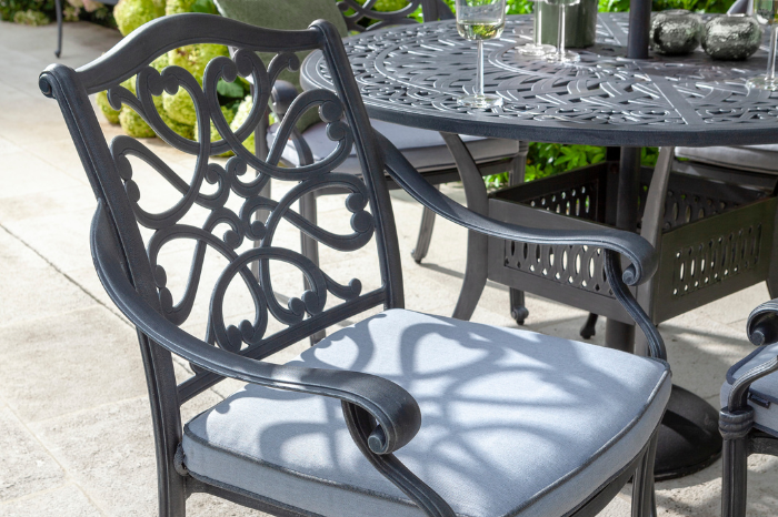 Outdoor patio chair with intricate back design and light gray cushion on a patio setting.