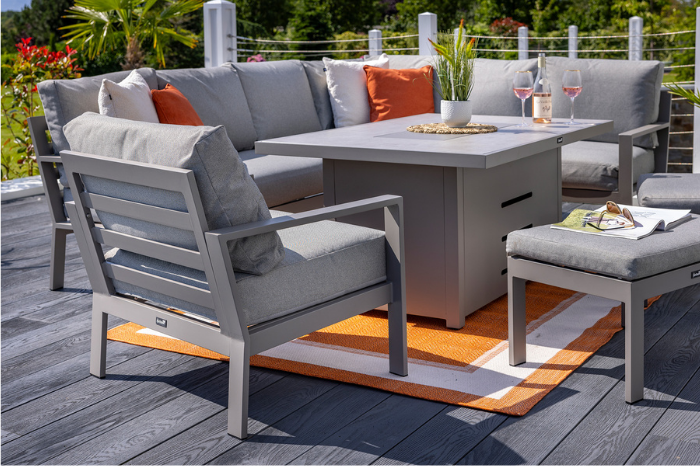 Outdoor patio furniture set with gray chairs, orange and white cushions, and a fire pit table on a wooden deck.