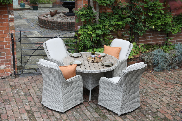 Outdoor patio set with four chairs and a round table in a garden setting.